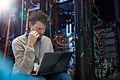 Focused IT technician using laptop in server room