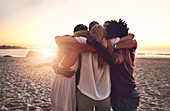 Young friends hugging in a huddle on sunset beach