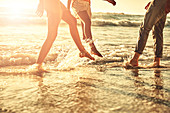 Young friends splashing in sunny summer ocean surf
