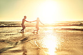 Young couple holding hands, walking in beach surf