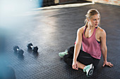 Young woman stretching, twisting next to dumbbells