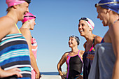 Smiling female swimmers talking on sunny beach