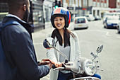 Smiling woman on motor scooter talking to friend