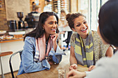 Smiling women friends talking at cafe table