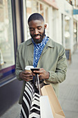 Smiling man texting on urban sidewalk