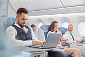 Businessman working at laptop on airplane