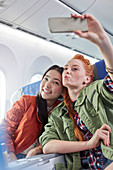 Young women friends posing for selfie on airplane