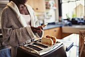 Woman texting, toasting bread in toaster
