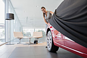 Car saleswoman removing cover from car in showroom