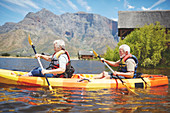 Active senior couple kayaking on sunny summer lake