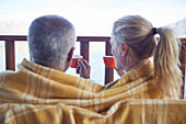 Cosy couple wrapped in blanket, drinking coffee