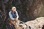 Male rock climber rappelling, descending from rope