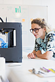 Female designer watching 3D printer in office