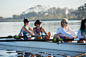 Female rowing team rowing scull on sunny lake
