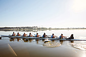 Female rowing team rowing scull on sunny lake