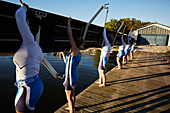 Female rowers lifting scull on sunny lakeside dock