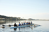 Female rowers rowing scull on lake below blue sky
