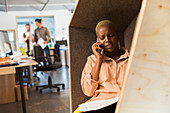 Businesswoman talking on smart phone in office cubby