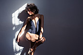 Female dancer stretching leg in sunlight at wall