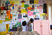Toddler brother and sister hanging art on wall