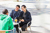 Smiling male friends talking at sidewalk cafe