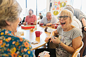 Happy senior woman playing cards with friend