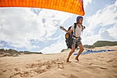 Male paraglider running with parachute on beach