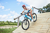 Man mountain biking down obstacle course ramp