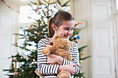 Girl hugging teddy bear in front of Christmas tree