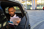 Businessman reading paperwork in crowdsourced taxi