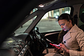 Businesswoman with smart phone in car at night