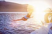 Woman jumping off boat into sunny ocean