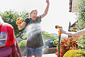 Daughter spraying mother washing car with hose