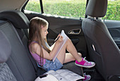 Girl doing homework in back seat of car