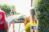 Playful daughter spraying mother with hose