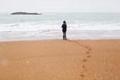 Teenage boy standing on snowy winter ocean beach