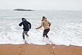 Brother and daughter playing in winter ocean surf