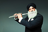 Well-dressed senior man in turban playing flute