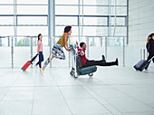 Playful couple pushing luggage cart in airport