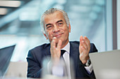 Smiling, senior businessman clapping in meeting