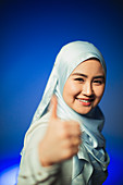 Young woman in blue silk hijab gesturing thumbs-up