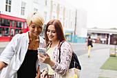 Young women friends texting on urban street