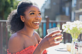 Happy woman drinking orange juice on sunny balcony