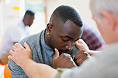 Man comforting young man in group therapy