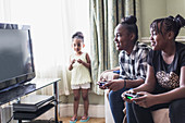 Toddler girl watching tween sisters playing video game