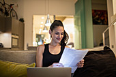 Woman reading paperwork at laptop