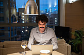 Man using laptop and drinking white wine at night