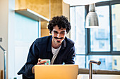 Smiling man drinking coffee, working at laptop