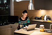 Focused woman using laptop and drinking white wine
