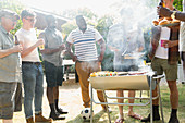 Male friends drinking beer and barbecuing in backyard